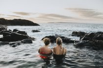 Mujeres sentadas en el agua y mirando el paisaje marino - foto de stock