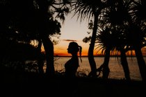 Жінка стоїть на пляжі з морським пейзажем під час заходу сонця — стокове фото