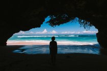 Женщина стоит в естественной пещере и смотрит на морской пейзаж — стоковое фото