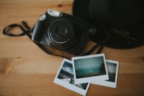 Camera, instant photos and hat on desk — Stock Photo
