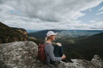 Femme assise sur le rocher et regardant le paysage — Photo de stock