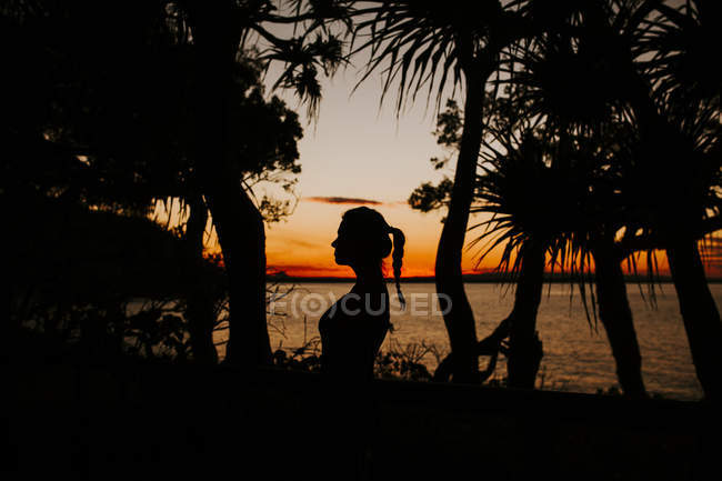 Frau steht bei Sonnenuntergang am Strand mit Meerblick — Stockfoto