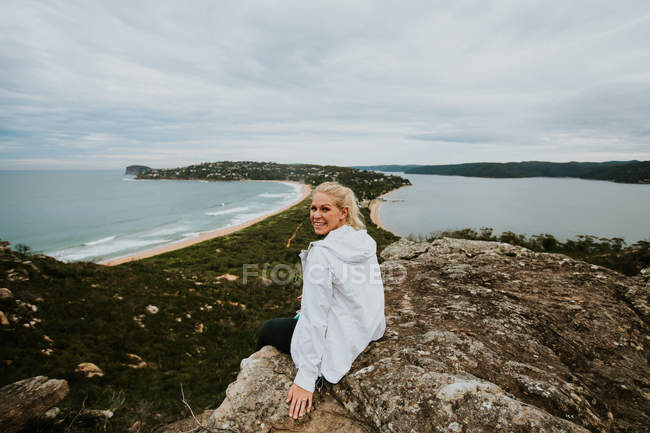 Mujer sentada en la roca y mirando un hermoso paisaje - foto de stock