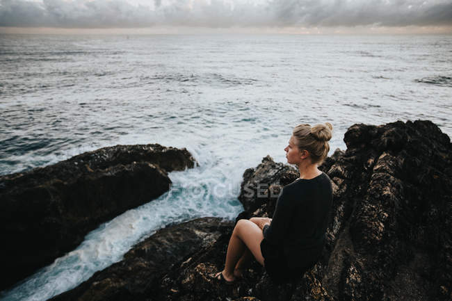 Женщина сидит на скале и смотрит на пейзаж — стоковое фото