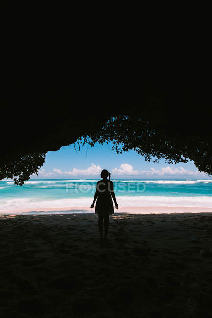 Женщина стоит в естественной пещере и смотрит на морской пейзаж — стоковое фото