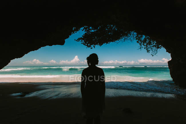 Frau steht in natürlicher Höhle und blickt auf das Meer — Stockfoto