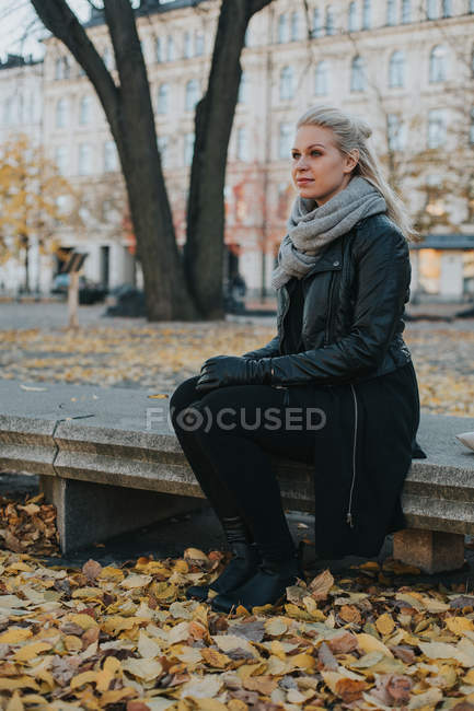Mujer sentada en el banco en el parque de la ciudad - foto de stock