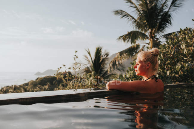 Donna in piscina guardando paesaggio marino — Foto stock