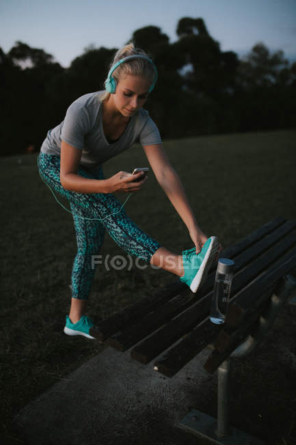 Mujer deportiva estirándose en el banco en la colina - foto de stock