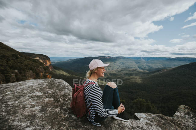 Mujer sentada en la roca y mirando el paisaje - foto de stock