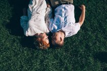Braut und Bräutigam liegen im Gras und schauen einander an — Stockfoto