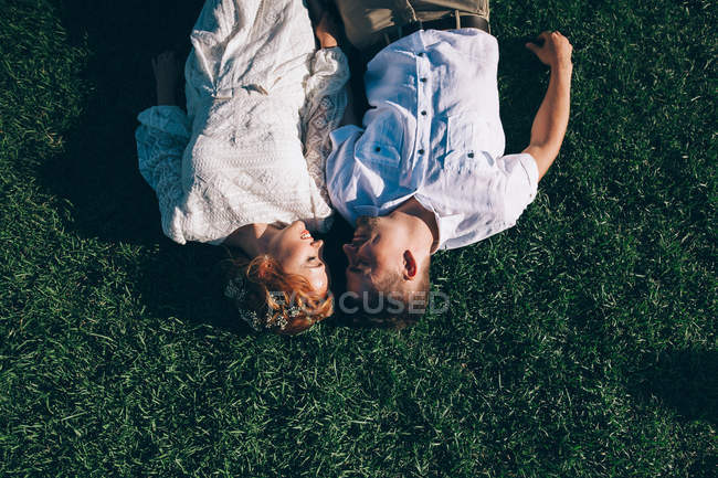 Mariée et marié couché sur l'herbe et se regardant — Photo de stock