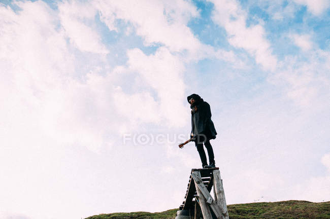 Mann mit schwarzer Kapuze und Gitarre steht am Ende des Holzstegs — Stockfoto