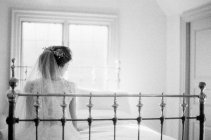 Femme en robe de mariée assise sur le lit — Photo de stock