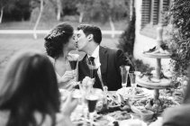 Newlyweds kissing at wedding table — Stock Photo