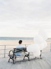 Hombre en el banco con globos en la orilla del mar - foto de stock