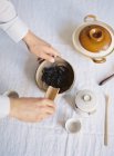 Mani che aggiungono foglie di tè nella teiera — Foto stock