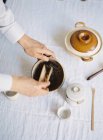 Руки добавляют листья чая в чайник — стоковое фото