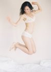 Женщина в изысканном белье прыгает на кровати — стоковое фото