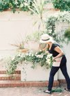 Задний вид женщины в шляпе, заботящейся о горшках с растениями на стене — стоковое фото