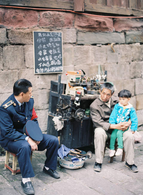 Policial chinês sentado com homem e criança — Fotografia de Stock