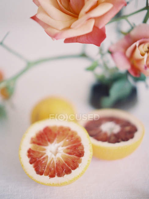 Laranja cortada pela metade fresca com rosas — Fotografia de Stock