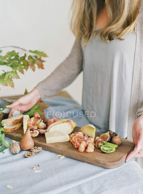 Woman holding board with cheese and fruits — Stock Photo