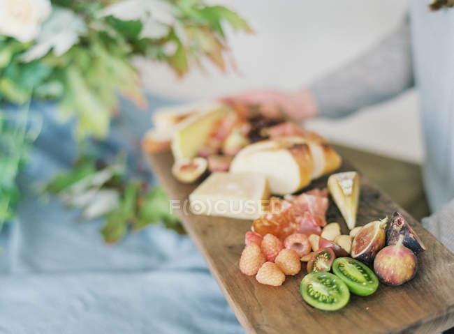 Woman holding board with cheese and fruits — Stock Photo