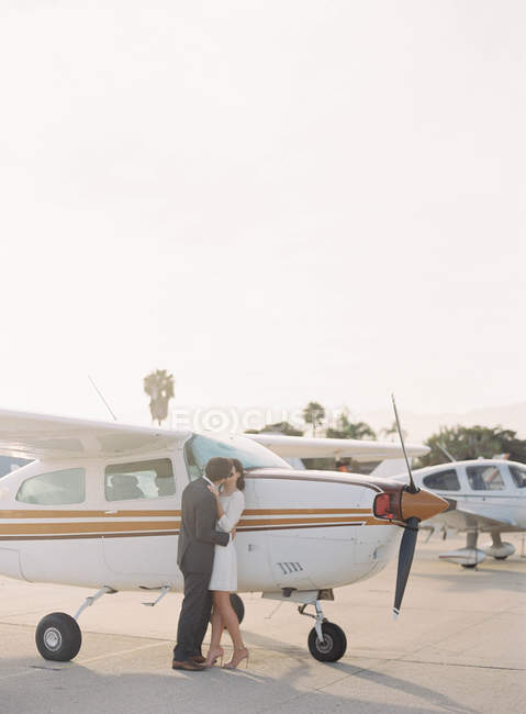 Пара обнимается и целуется рядом с самолетом — стоковое фото