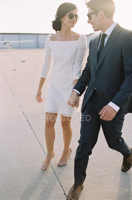 Couple walking holding hands at airfield — Stock Photo