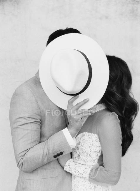 Couple embracing and covering faces with hat — Stock Photo