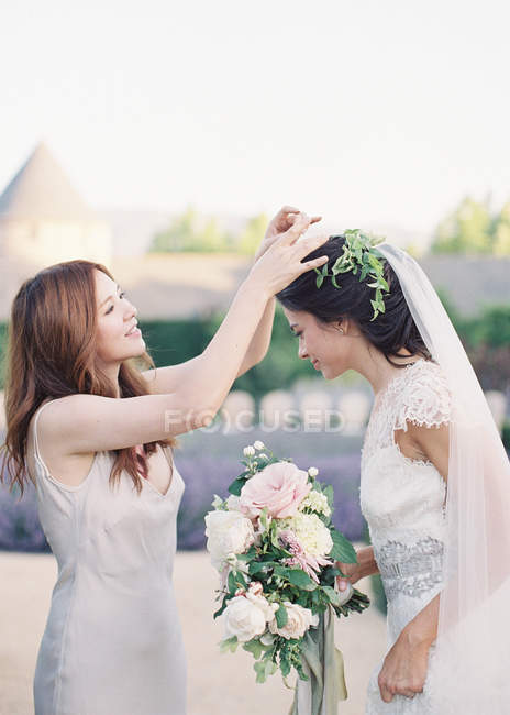 Bridesmaid helping beautiful bride with veil — Stock Photo