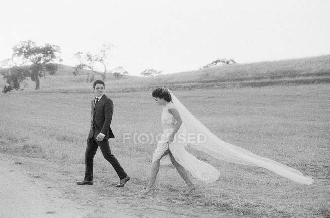 Newly wed couple walking in field — Stock Photo