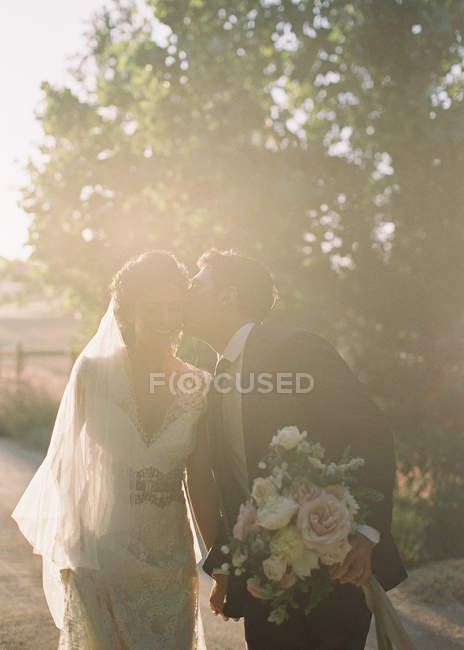 Groom kissing bride while outdoor — Stock Photo