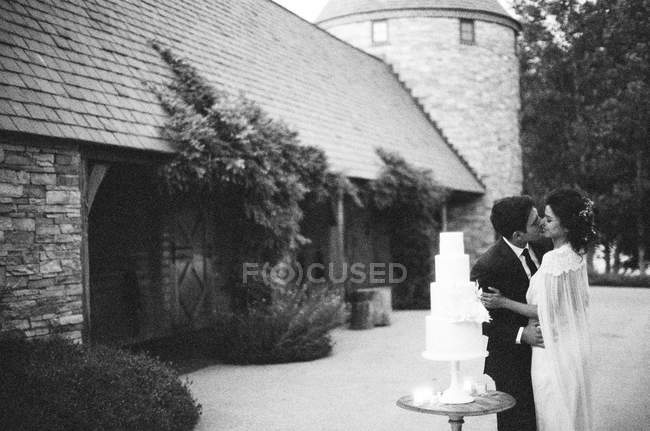 Пара целуется рядом со свадебным тортом — стоковое фото