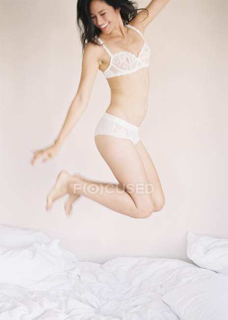 Frau in exquisiter Dessous springt auf Bett — Stockfoto