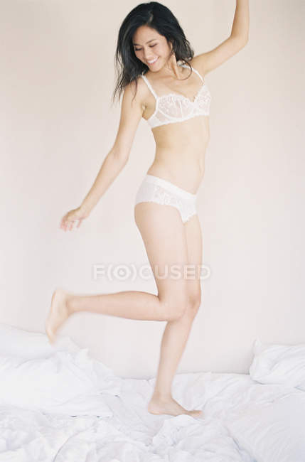 Femme en lingerie exquise sautant sur le lit — Photo de stock