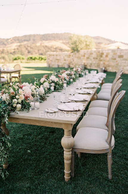 Wedding table with flowers and rows of chairs — Stock Photo