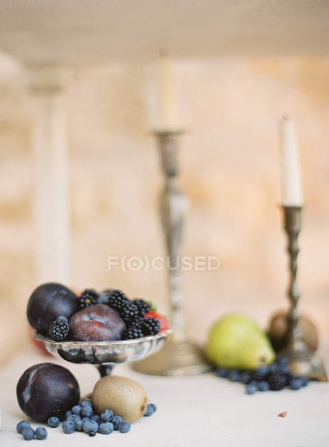 Fresh plums and berries in antique stand — Stock Photo