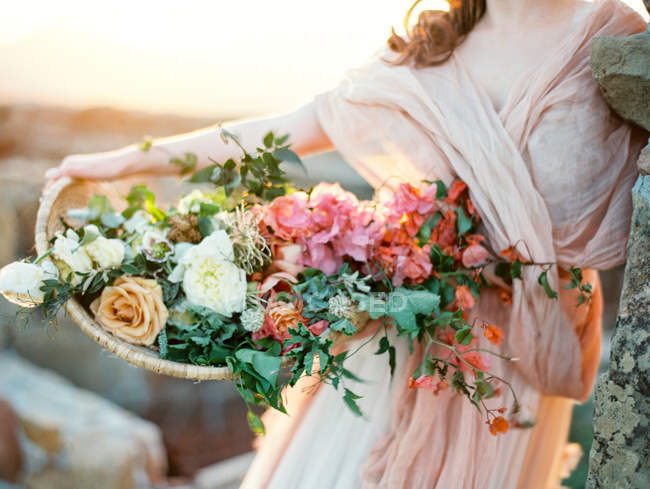 Женщина в завуалированном платье держит корзину с розами — стоковое фото