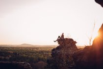 Женщина сидит на скале и смотрит на лес — стоковое фото