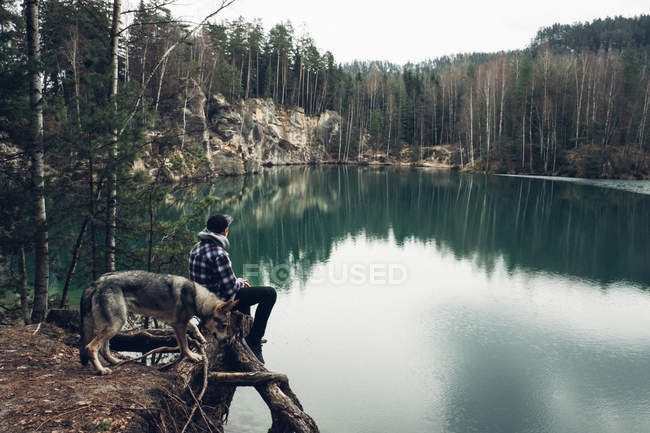 Young man with dog sitting on cliff — Stock Photo