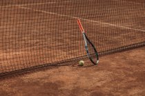 Bola de tênis e raquete inclinados na rede — Fotografia de Stock