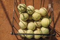 Cesta de pelotas de tenis de pie en la superficie de la cancha naranja - foto de stock
