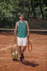 Tennis player carrying basket of balls on court — Stock Photo