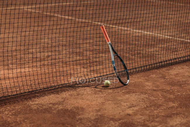 Pelota de tenis y raqueta apoyada en la red - foto de stock