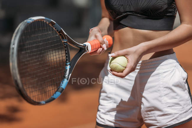 Обрезанный снимок спортивной молодой женщины с теннисной ракеткой и мячом — стоковое фото