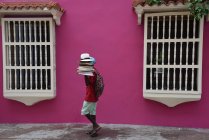 Seller walking with hats by pink building — Stock Photo