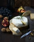 Closeup view of cheese wheel with bread slices, walnuts and pomegranate on wood — Stock Photo
