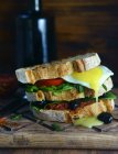 Closeup view of big sandwich with greenery, fried egg, stuffing and olives on wooden board — Stock Photo